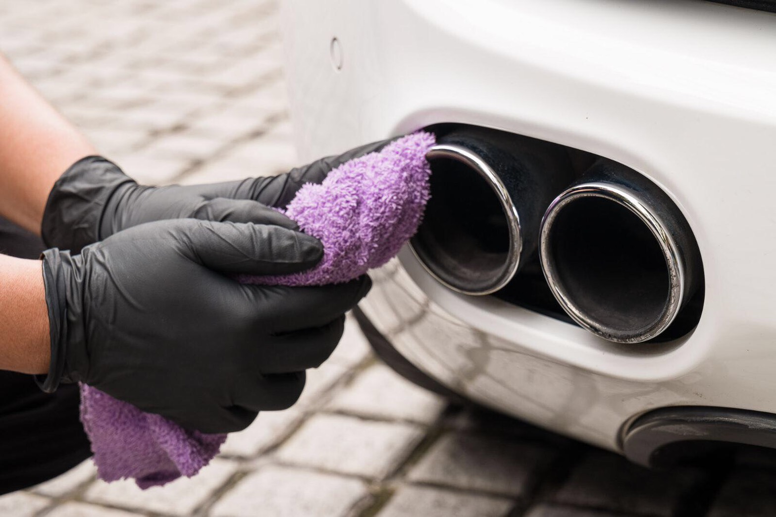 Gloved hands polishing chrome exhaust tips with a purple microfibre towel