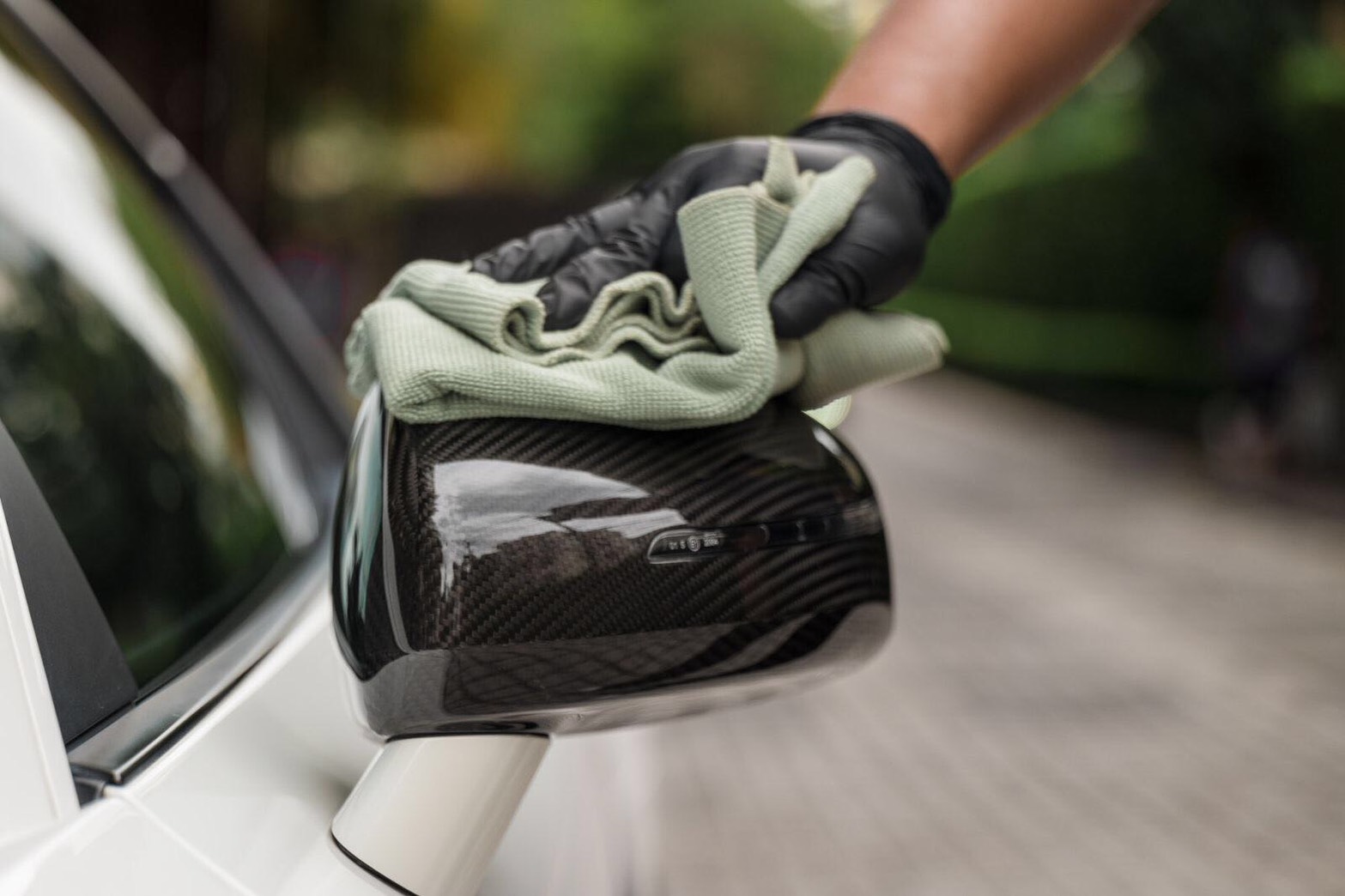 Gloved hand buffing a glossy carbon-fibre wing mirror with a microfibre cloth