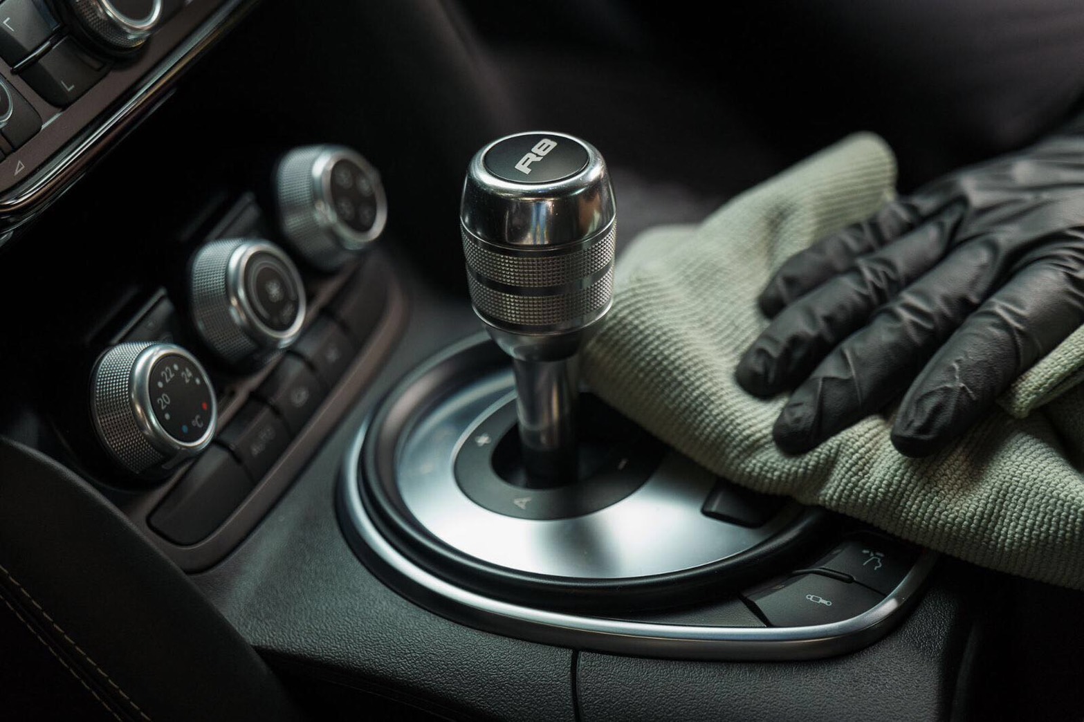 Gloved hand cleaning around a polished gear shifter and climate controls